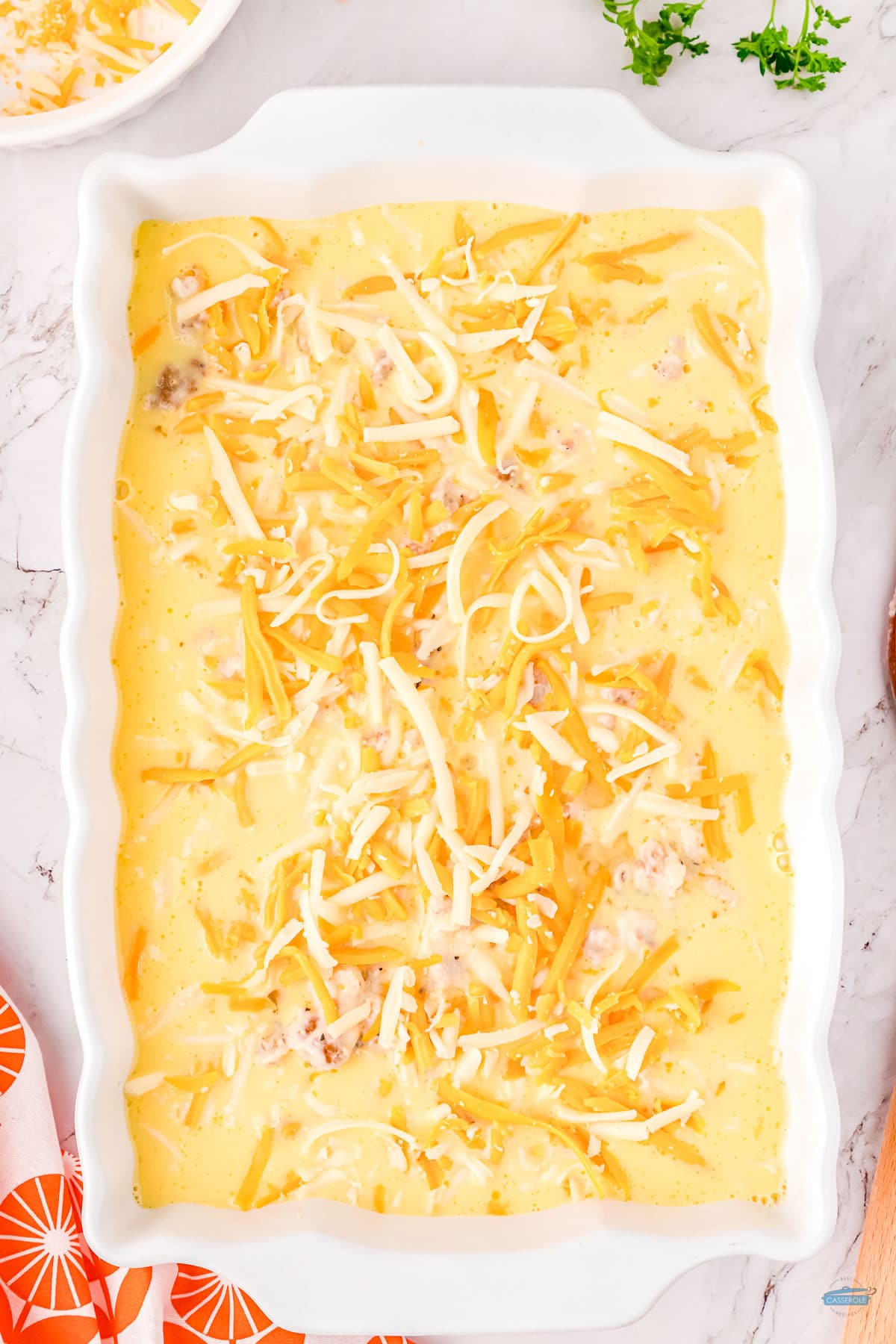 unbaked casserole in a white dish with shredded cheese on top