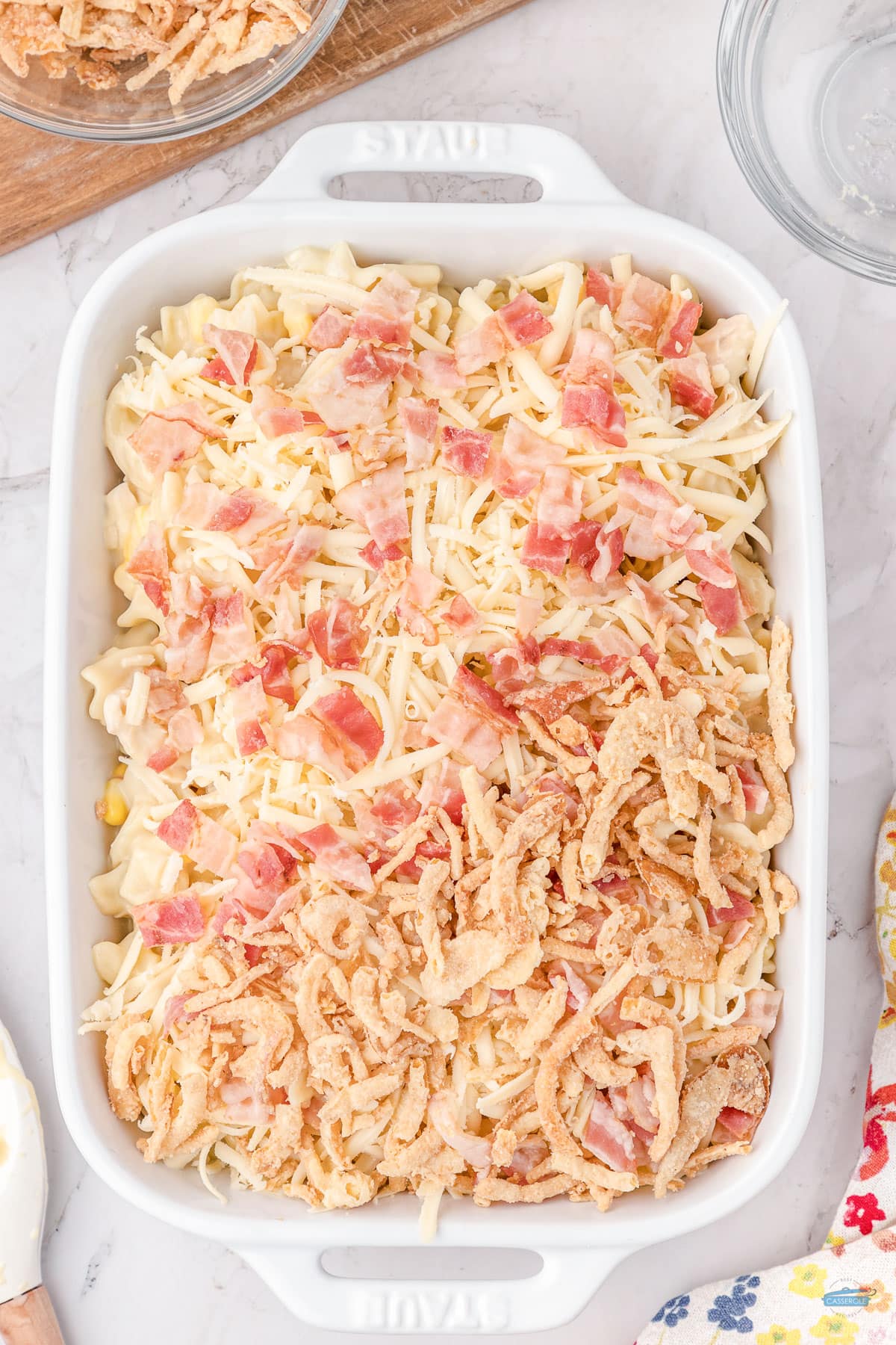 bacon and french fried onion on top of noodles in a casserole dish