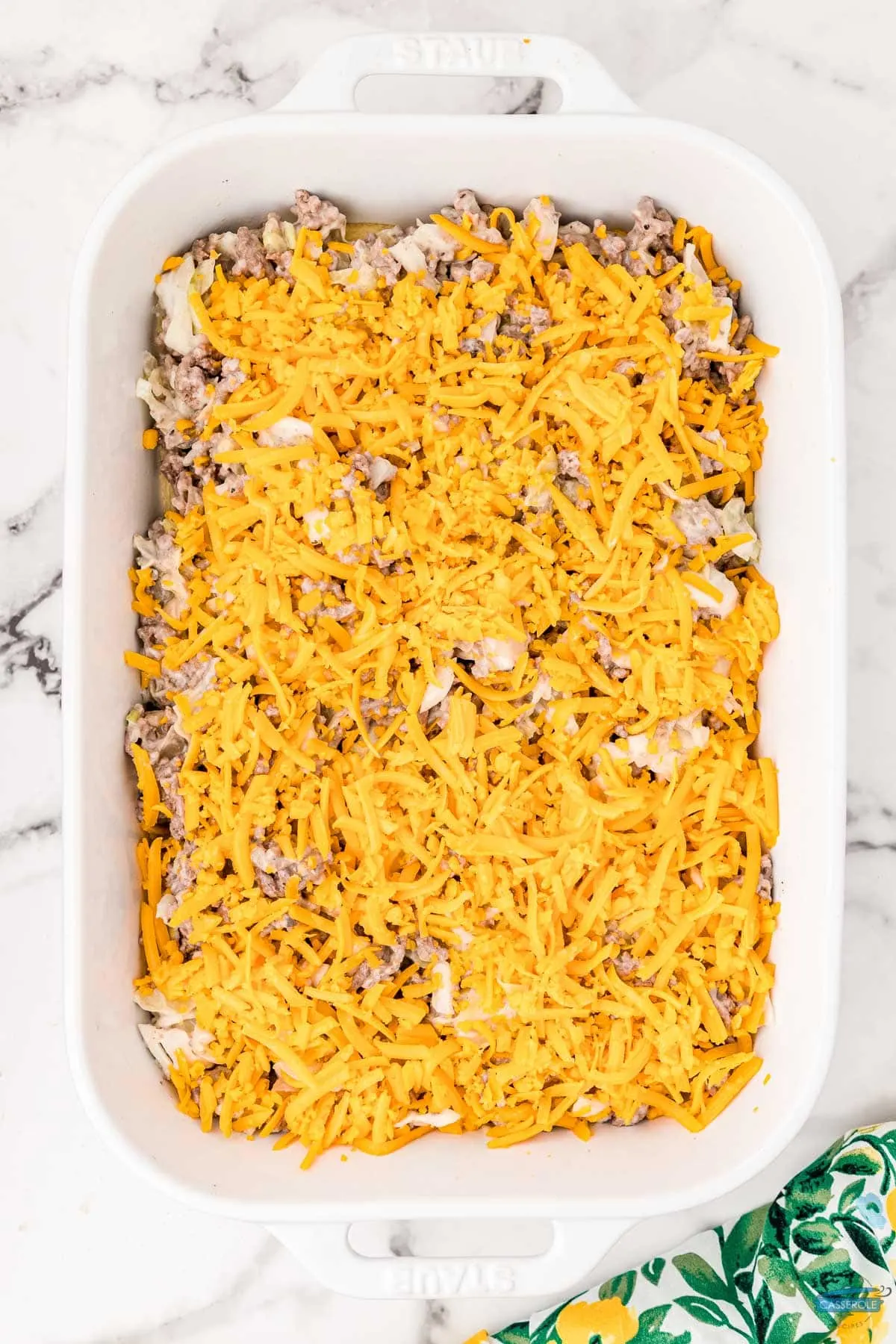 unbaked casserole covered in cheese in a white dish