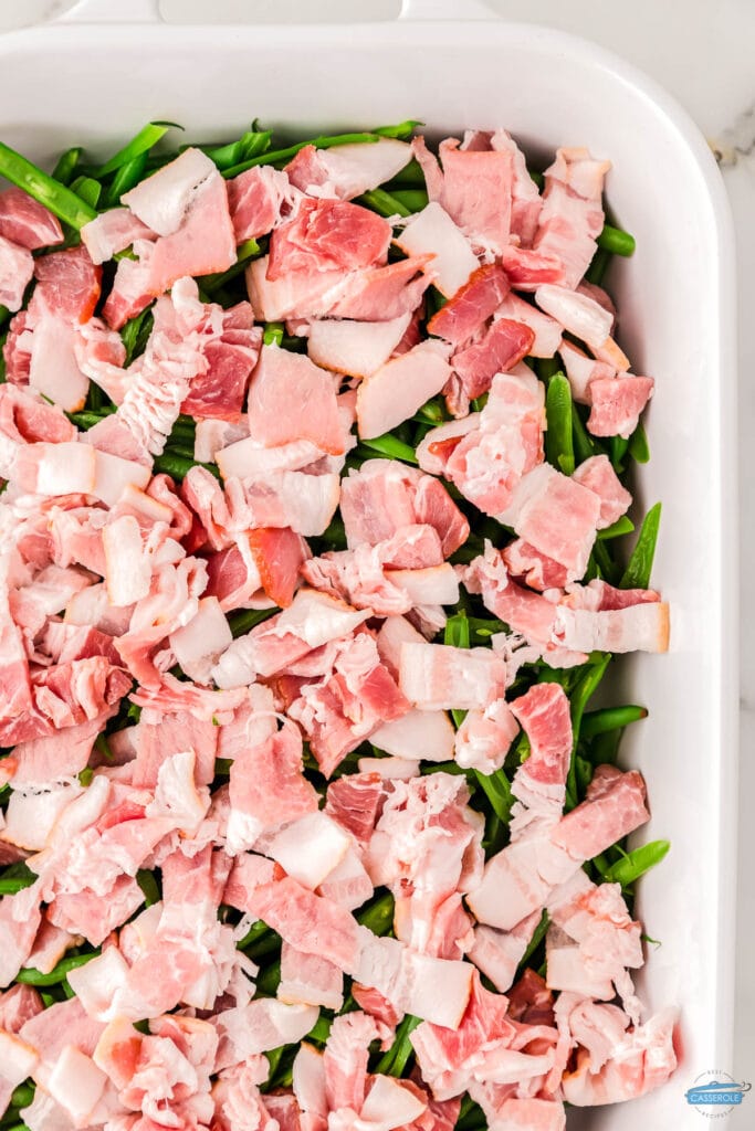 bacon pieces sitting on top of green beans in a white casserole dish