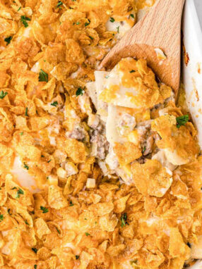 wood spoon scooping out casserole topped with corn flakes