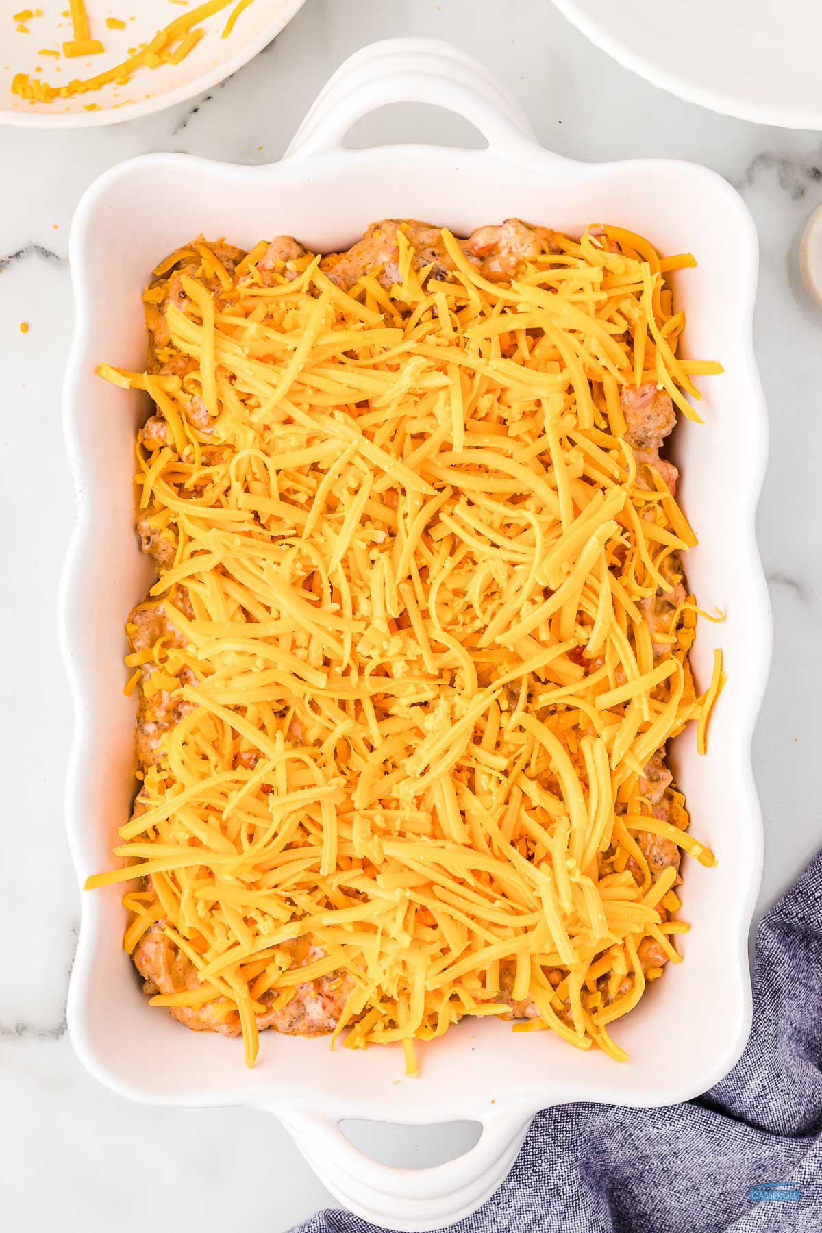 shredded cheese on top of casserole in a white rectangle dish