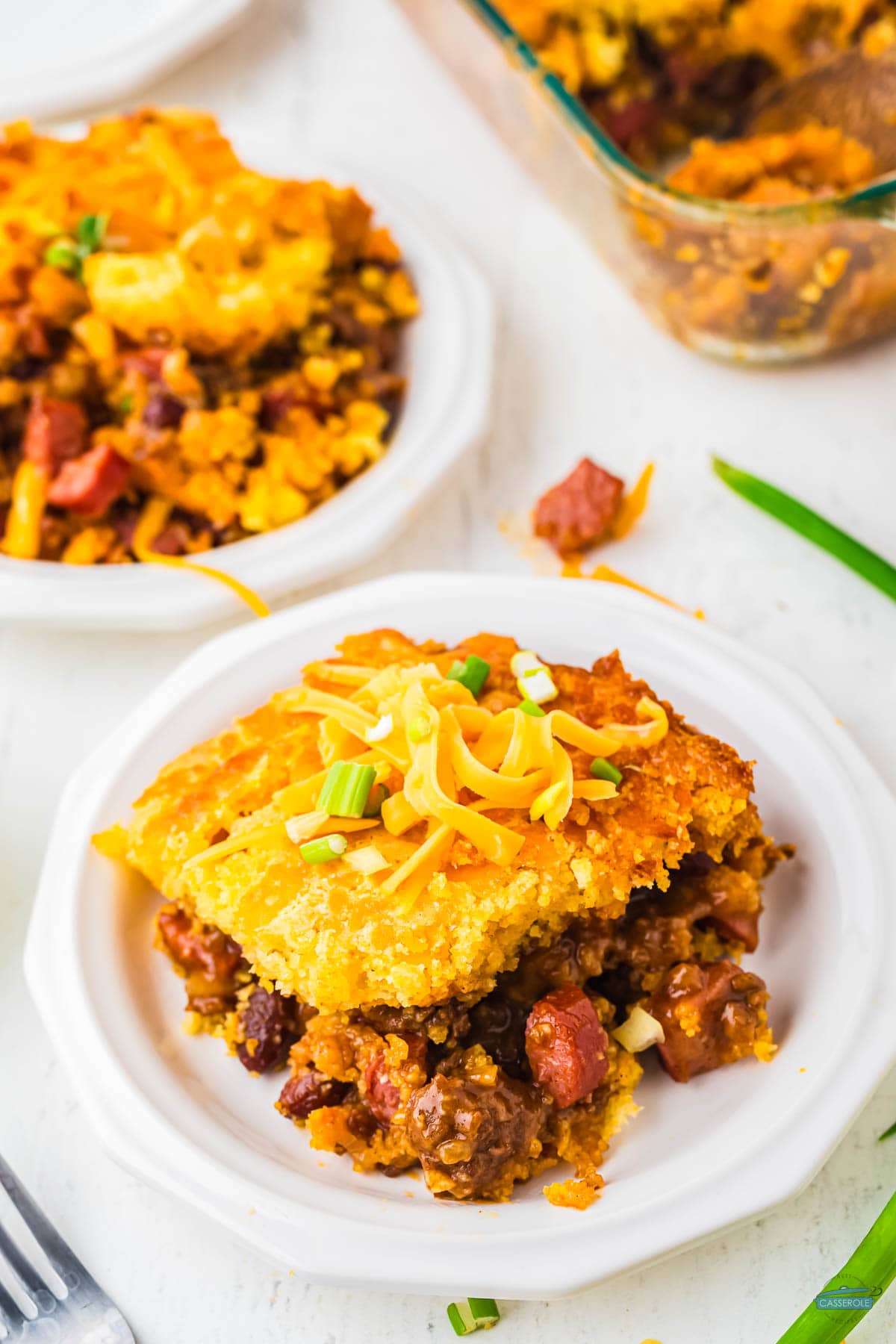 slice of casserole on a plate topped with green onions and cheese